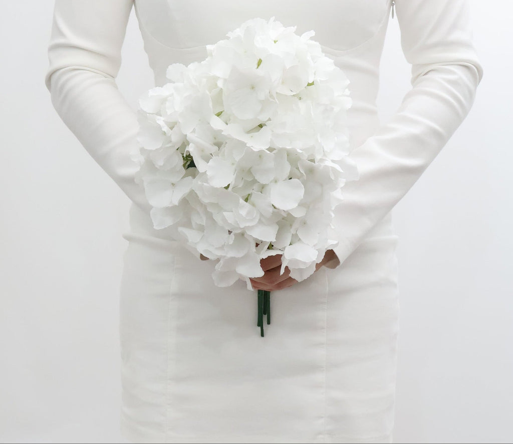 Bride holding a bouquet of white hydrangeas flowers against a plain background