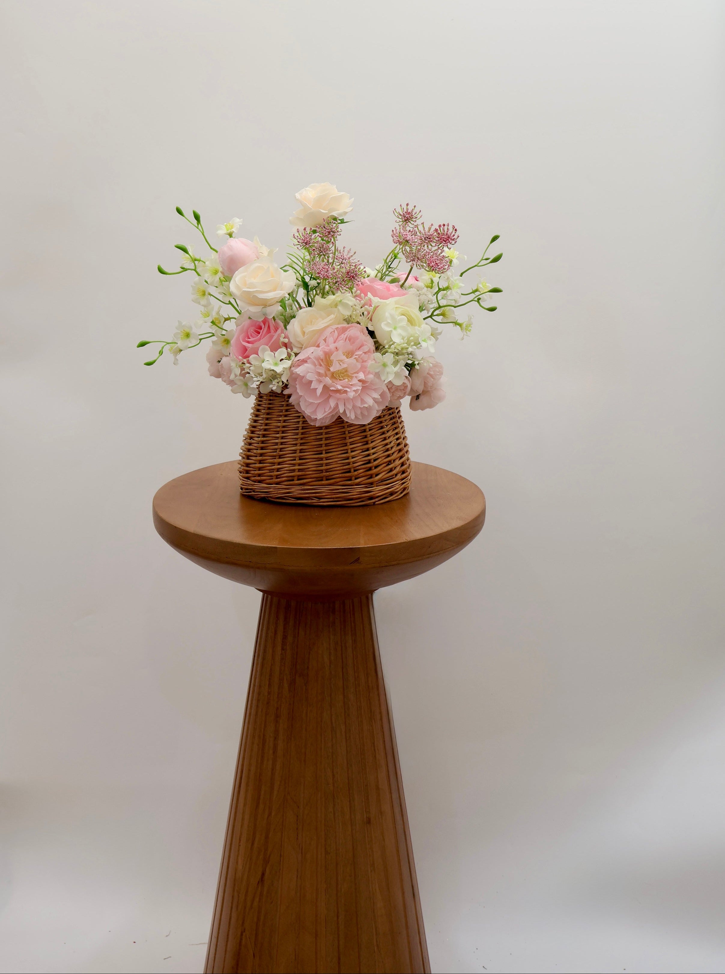 Trendy Bridesmaid basket bouquet with pastel flowers on a wooden stool against a white background