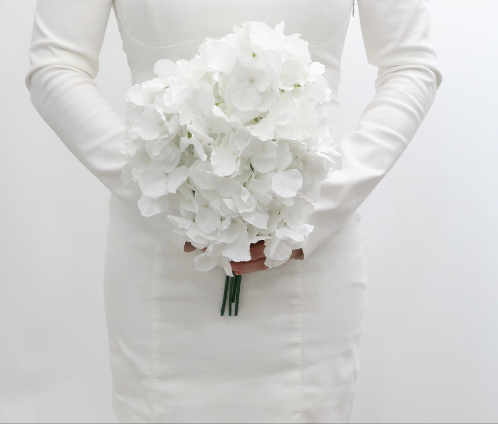 Bride holding a bouquet of white hydrangeas flowers against a plain background