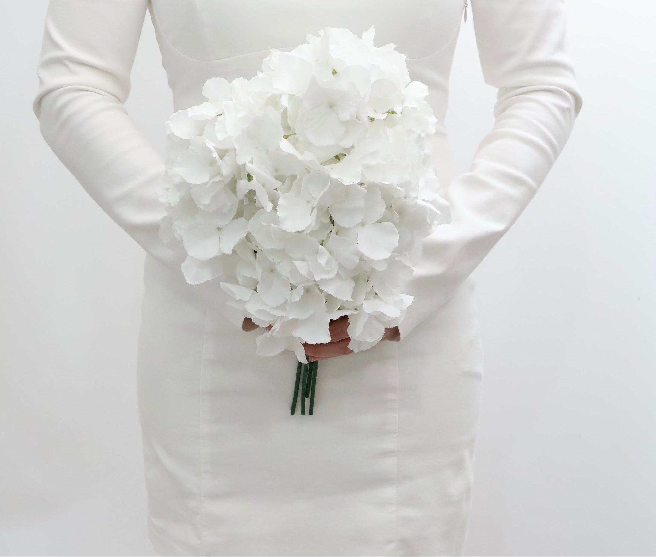 Bride holding a bouquet of white hydrangeas flowers against a plain background