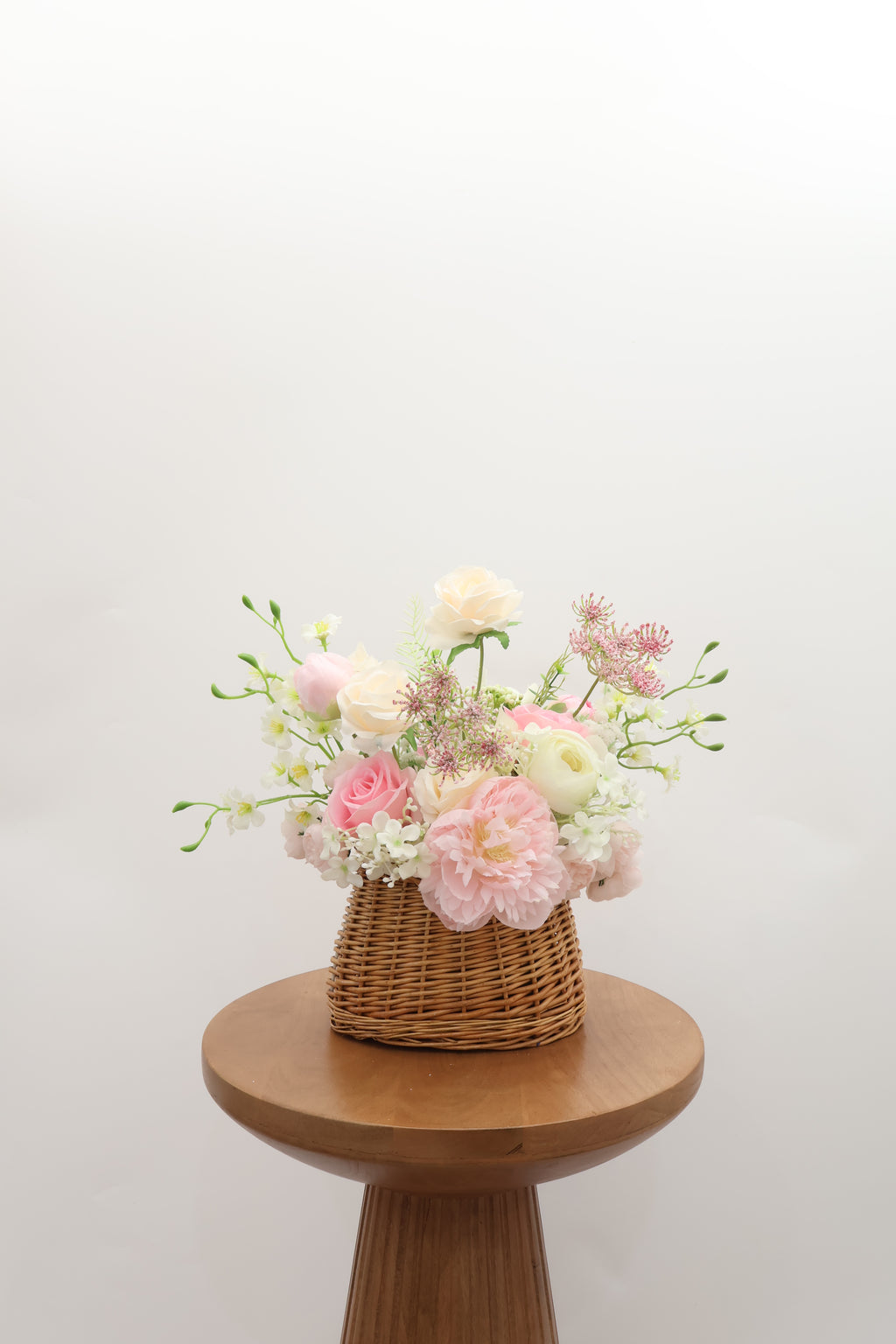 Trendy Bridesmaid basket bouquet with pastel flowers on a wooden stool against a white background