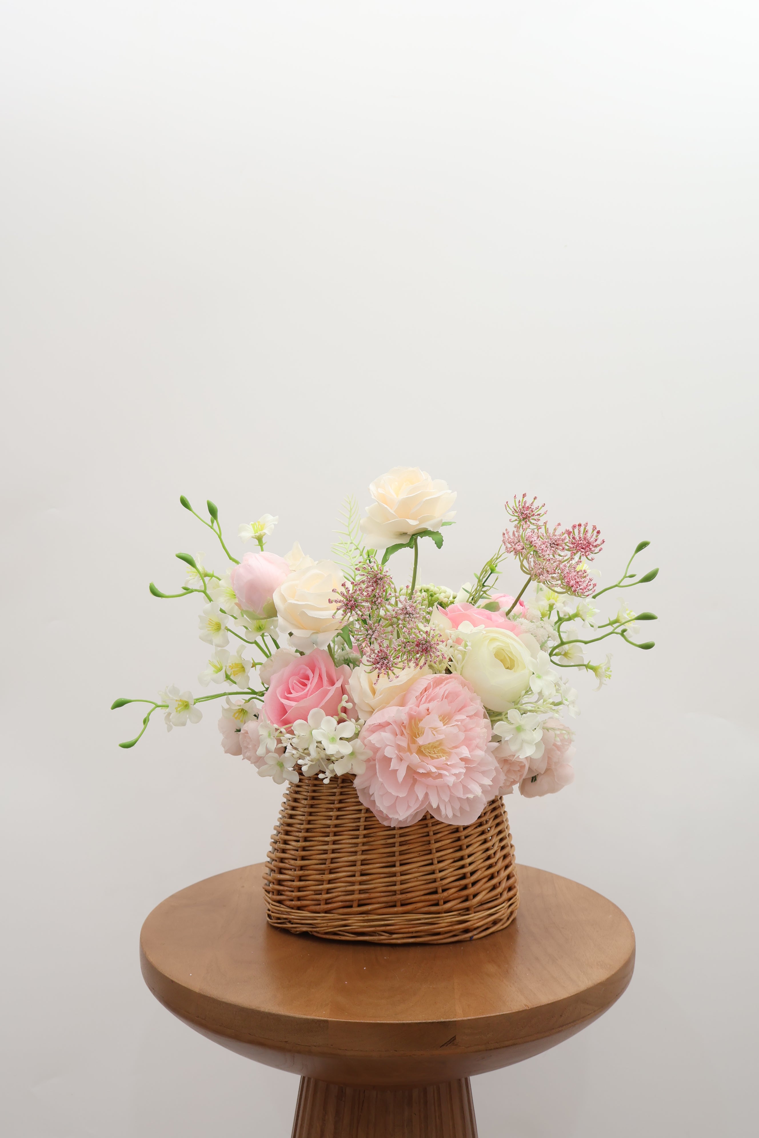 Trendy Bridesmaid basket bouquet with pastel flowers on a wooden stool against a white background