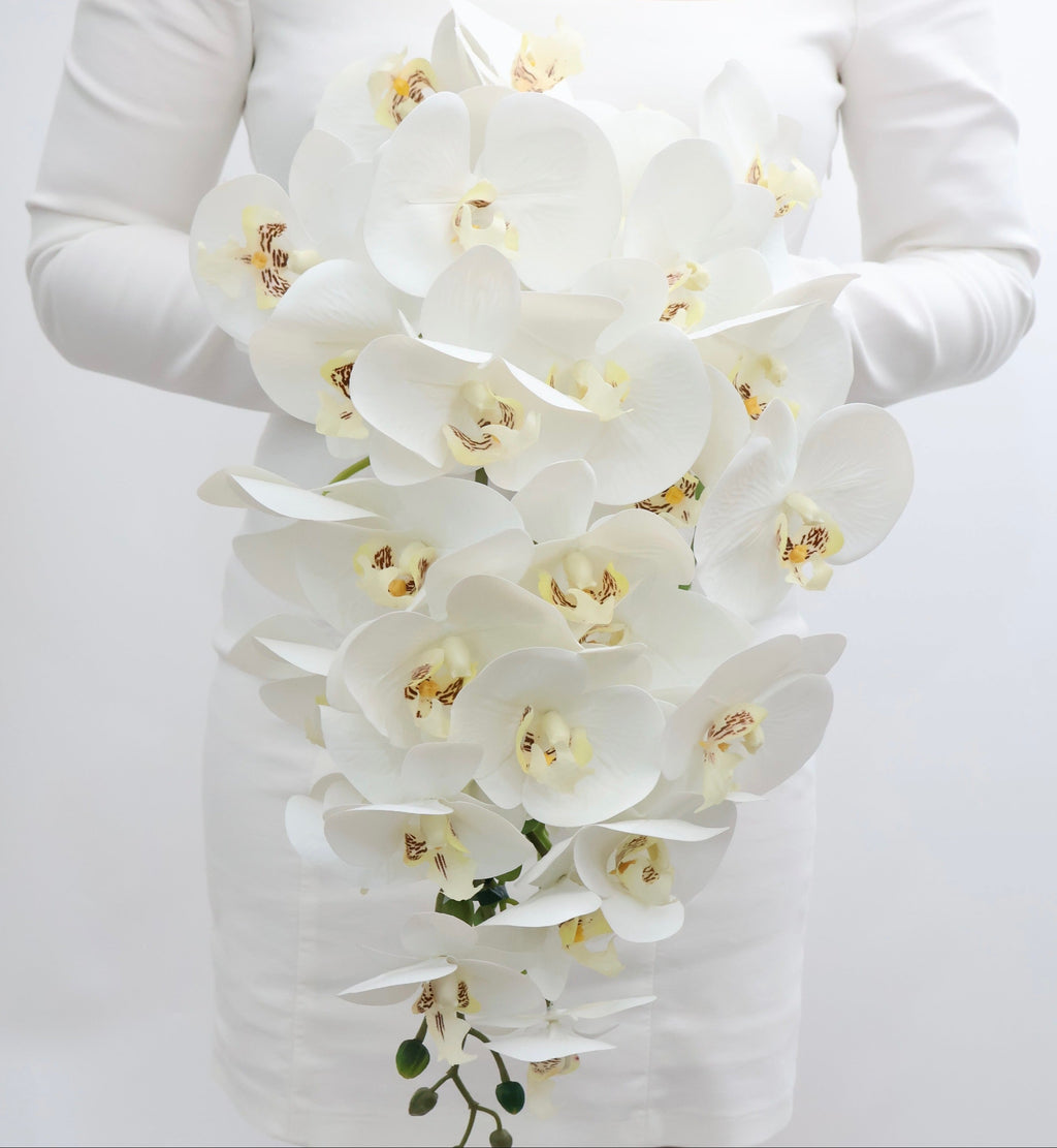 Bouquet of white cascading orchids held by a bride wearing a white long-sleeve dress.