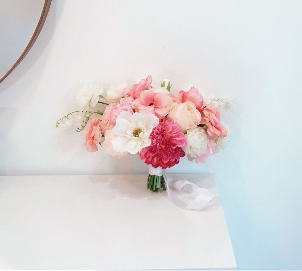 Bouquet of pink and white flowers on a white surface with a light blue wall in the background