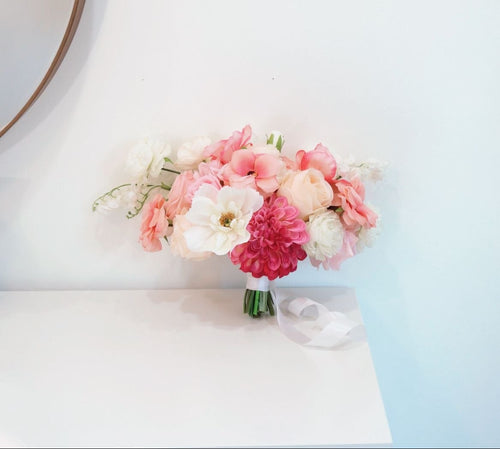 Bouquet of pink and white flowers on a white surface with a light blue wall in the background