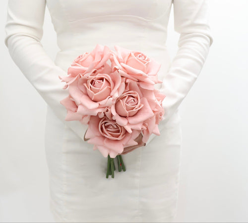 Bouquet of pink roses held by a person wearing a white long-sleeve bridal gown