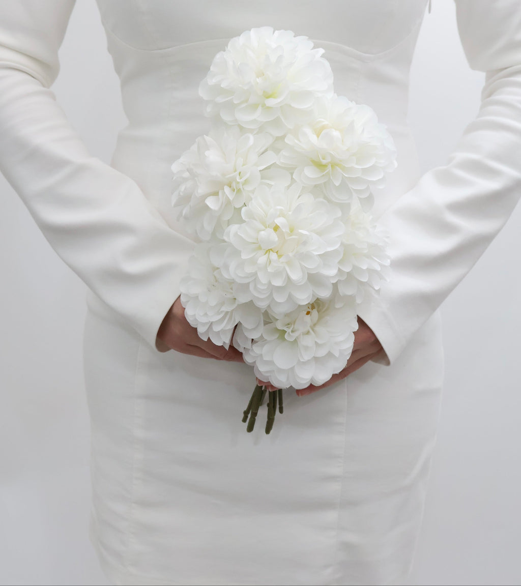 Bride holding a bouquet of white dahlia flowers against a plain background