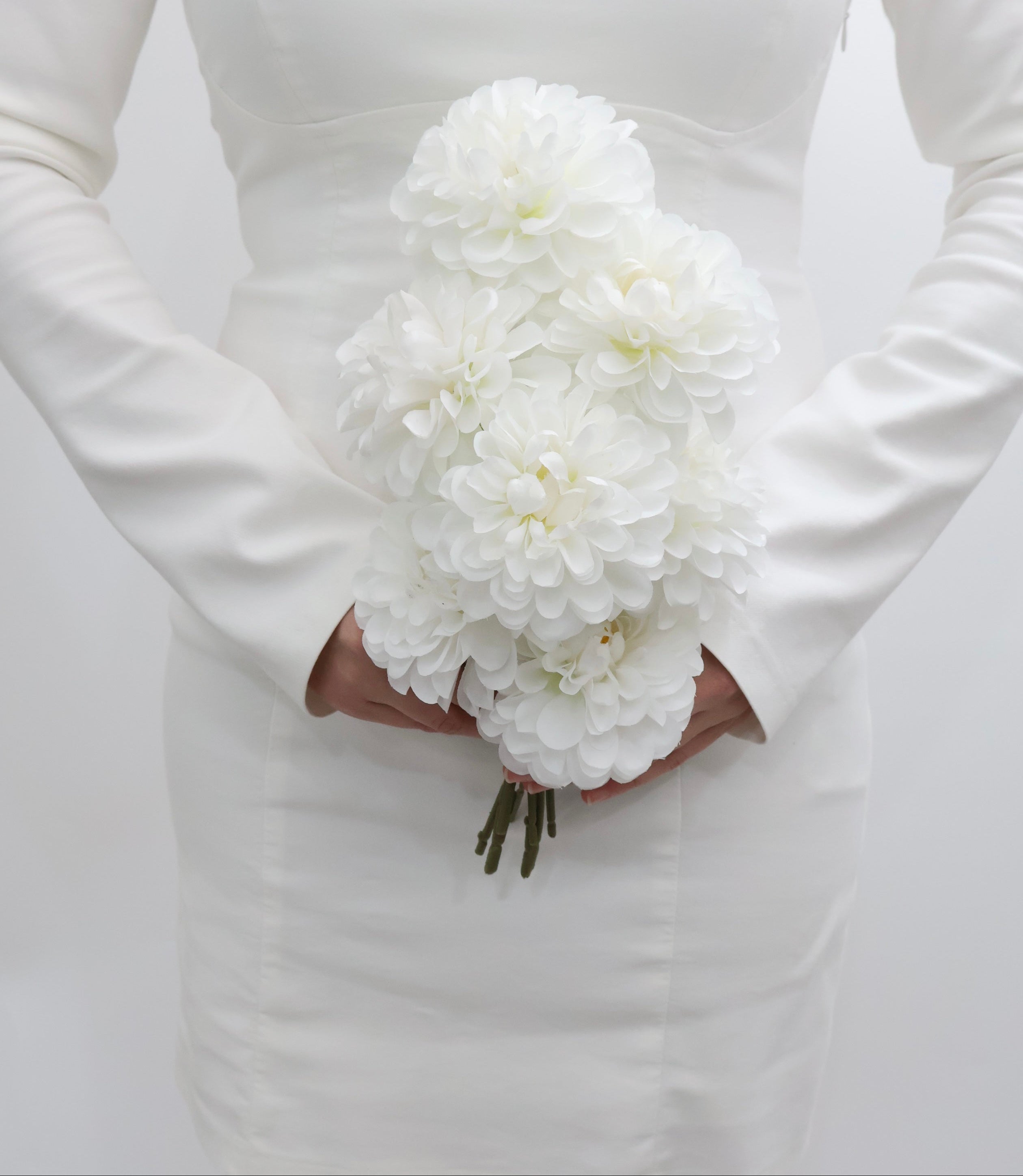 Bride holding a bouquet of white dahlia flowers against a plain background